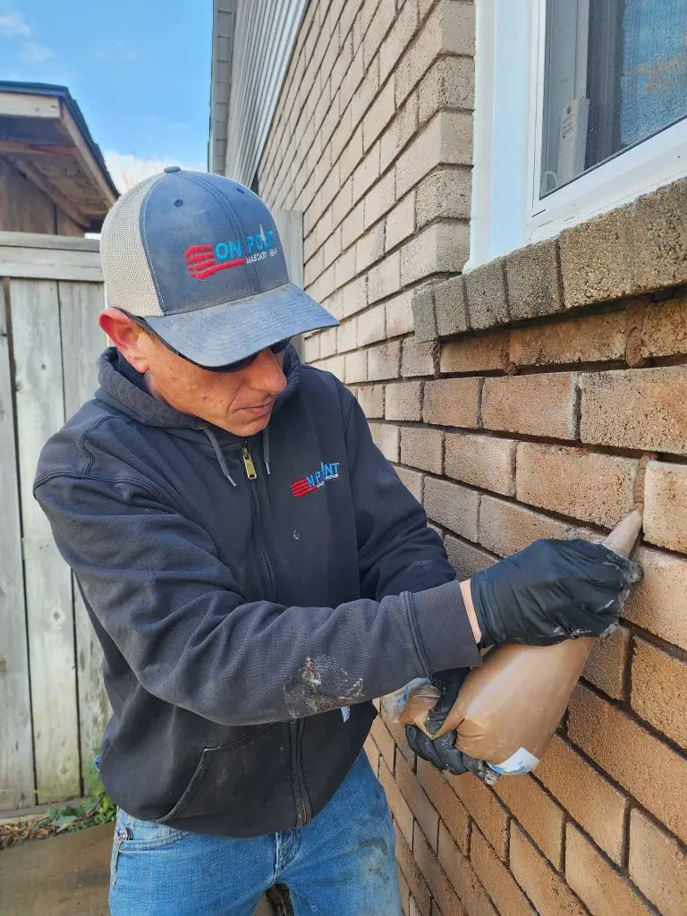 On Point mason repointing the brick joints beneath a window with a brick rowlock sill