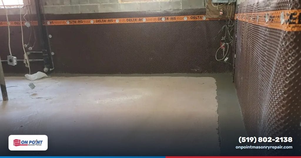 Basement wall lined with dimple drainage membrane above a freshly poured concrete channel that carries water to the sump pit